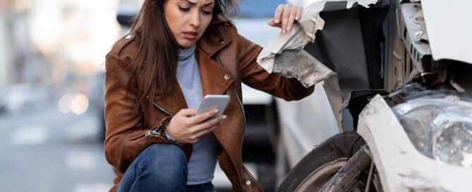 Sad young woman texting after car crash on road concerned about insurance points in NC